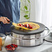 A person using a Carnival King 16" Non-Stick Round Portable Crepe Maker to cook a crepe with fruit.
