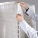 A person in a white lab coat using a Curtron translucent white plastic bag to cover a bun pan rack.