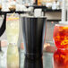 A glass table with a black and silver Arcoroc stainless steel bar shaker next to a white drink.