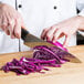 A person using a Victorinox chef knife to cut a red cabbage.