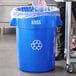 A man in a chef's uniform standing next to a blue Lavex Recycling Can with a plastic bag over it.