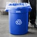 A man in a chef's uniform standing next to a blue Lavex recycling can with a plastic bag inside.