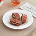 A Fineline white plastic plate with two slices of steak and a piece of bread.