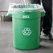 A man in a black suit recycling a water bottle in a green Lavex recycling can.