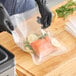A vacuum packaging pouch containing a piece of salmon, lemon slices, and herbs on a wooden surface.