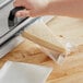 A person cutting cheese on a cutting board on a counter in a professional kitchen using a Choice vacuum packaging bag.