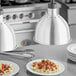 A plate of pasta with meatballs and sauce under a ServIt chrome heat lamp with a white dome shade.