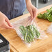 A clear vacuum packaging pouch containing green vegetables on a wooden surface.