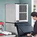 A woman standing in front of a large white and grey Scotsman Prodigy Plus air cooled ice machine.