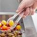 A person using Cambro clear plastic scallop grip tongs to serve yellow tomatoes.