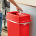 A person putting a plastic bag in a Lavex red rectangular trash can with a Drop Shot lid.