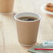 A close up of a Choice double wall paper hot cup filled with coffee with foam on a table.