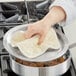 A hand holding a white towel over a Choice aluminum saute pan full of meatballs being cooked.