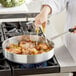 A person cooking food in a Choice aluminum saute pan on a stove.