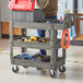 A man standing next to a Lavex medium gray utility cart with tools in it.