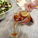 A person pouring brown liquid from a Fineline clear plastic pitcher into a glass.