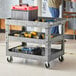 A man standing next to a Lavex large gray utility cart with tools on it.