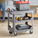A man standing next to a Lavex medium gray utility cart with tools in it.