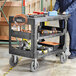 A man standing next to a Lavex large black utility cart with tools on it.