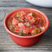 A cranberry melamine bowl of salsa on a wood table.