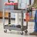 A man using a Lavex medium gray utility cart with tools on it.