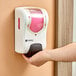 A person using a white and pink San Jamar Summit Rely manual foam hand soap and sanitizer dispenser.