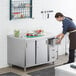 A woman in an apron opening drawers on a Regency stainless steel table in a kitchen.