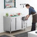 A woman in an apron using a Regency stainless steel table with drawers in a kitchen.