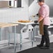 A man wearing a chef's hat and brown apron using a ServIt natural gas steam table in a professional kitchen.