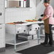 A man in a brown apron using a ServIt natural gas steam table on a counter in a kitchen.