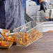 A person in a blue shirt and apron holding a 13 1/4" x 5 5/8" Fryer Basket full of french fries.