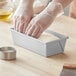 A person wearing plastic gloves kneading bread dough in a Baker's Mark aluminized steel bread loaf pan.