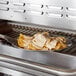 An oval aluminum sizzler platter with food cooking on it on a grill.