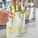 A hand holding an Acopa copper stainless steel bent straw over a glass of liquid.
