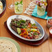 An oval aluminum sizzler platter on a table with food on it.