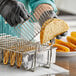 A person in black gloves using a Choice nickel-plated steel taco fry basket to hold tacos.