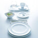 An Arcoroc white saucer with a white cup on a white table with white plates and silverware.