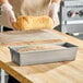A rectangular glazed aluminized steel bread loaf pan with a partially risen loaf inside, placed on a wooden countertop.