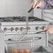 A hand using a 10" x 4 3/4" metal fryer basket press to hold a basket of food over a frying pan.