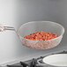 A person holding a Choice fine mesh culinary basket over a pan on a stove.