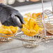 A person in black gloves uses a Choice Tortilla Double Taco Cup Fry Basket to fill a tortilla shell with chips.