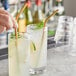 A hand holding an Acopa gold stainless steel reusable bent straw over a glass of liquid.