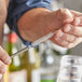 A person uses an Acopa stainless steel straw cleaning brush to clean a metal straw on a counter in a cocktail bar.