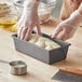 A person wearing gloves prepares dough in a Choice bread loaf pan.