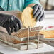 A person in black gloves using a Choice nickel-plated steel tostada fry basket to fry a tortilla.