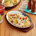 Two oval aluminum sizzler platters with nachos and sauces on a table in a Mexican restaurant.