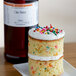 A cake with sprinkles on top and LorAnn Oils Cake Batter flavor displayed on a counter.