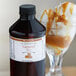 A bottle of LorAnn Oils Caramel Super Strength Flavoring liquid next to a glass of ice cream.