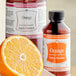 A bottle of LorAnn Oils all-natural orange bakery emulsion next to half an orange.