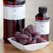 A bowl of purple candies next to a bottle of LorAnn Oils Plum Super Strength Flavor.